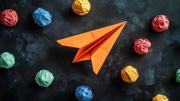 An orange paper airplane surrounded by colorful crumpled paper photo