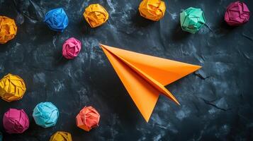 An orange paper airplane surrounded by colorful crumpled paper photo