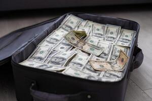 an old black suitcase with an open lid full of one hundred dollar bills. Corruption photo