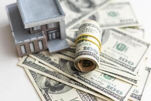 A small house lies on a fan of hundred dollar bills. The keys to the purchased house. Reduced copy of the house on a white background photo