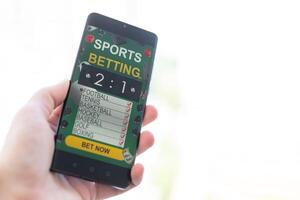 Man betting on sports using smartphone and laptop at table, closeup. Bookmaker websites on displays photo