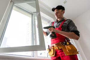 Professional installer of plastic windows poses in a working uniform, holds glasses with his hand. Specialist in the installation of plastic windows looks into the camera with a serious look photo