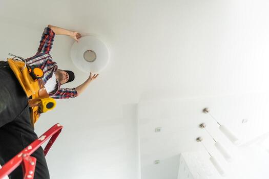 An electrician installs a chandelier on the ceiling. Hands of an electrician installing and connecting a lamp to a ceiling. photo