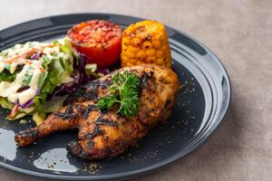 Half chicken baked in a sauce of garlic, soy, ginger, and honey. plate with baked corn, salad and tomatoes. photo