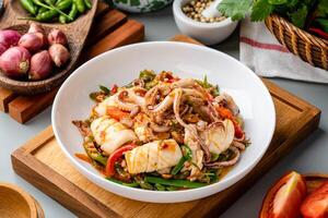 Tumis Cumi tauco or Spicy Stir Fried Squid with tauco Served on white plate and isolated on gray background. Tauco is a paste made from preserved fermented yellow soybeans. photo