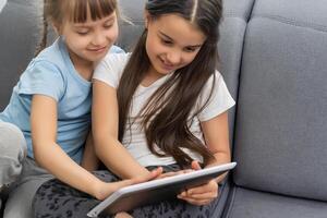 Two little sisters using tablet at home. Watching something funny. photo