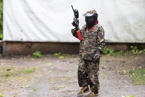 Paintball game. Players with weapons shooting paint balls. Men on the playground. Guys in camouflage and masks are fighting. photo