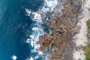 overhead drone view of waves splashing in a rocky shore photo