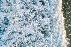 drone top view of seawater foam on the shore of a beach, beach background texture photo