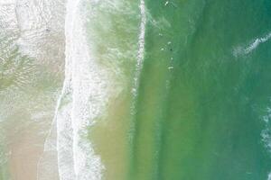 zenithal view of the shore of a beach in summer, with people surfing in the waves on the shore. Drone aerial view photo
