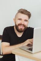Happy smiling young man watching and working on computer laptop at home. Technologies, remote work and social networks photo