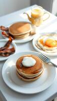 Stack of Pancakes with Butter and Syrup, Fried Egg, and Bacon on a White Table photo