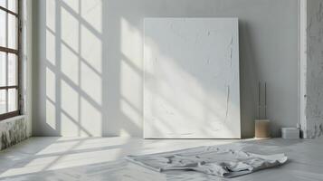 Gallery corner with sunlight illuminating white canvas leaning against wall and white cloth on floor photo