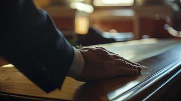 Man in a formal black suit is leaning his hand on a shiny wooden table in a courtroom photo