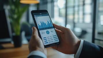 Businessman using a smartphone to analyze financial charts and data for decision-making in a contemporary office setting photo
