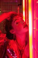 Fashion model strikes a glamorous pose under vibrant red neon lights, exuding style and sensuality in a trendy urban setting, perfect for a night out photo