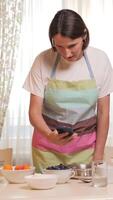 vertical Female home cook using smartphone while preparing ingredients video