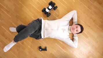 top view of a man lying on his back on the floor, model of rc car stands nearby video