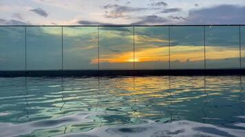A tranquil rooftop infinity pool reflects the vibrant colors of a stunning sunset, creating a serene and peaceful atmosphere perfect for relaxation and luxury travel, A tranquil sunset over pool video
