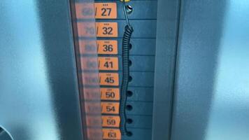 a weight stack on a gym machine, showing a series of rectangular weight plates with orange labels indicating different weights in kilograms, modern gym equipment, details of the weight plates video