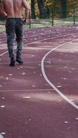 espalda ver de un hombre trotar en el estadio. joven atleta practicas corriendo fuera de en atletismo pista en otoño. vertical video