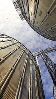 Grain elevators under blue sky. Huge metal grain storage tanks. Silver containers. Close-up. View from below. Vertical video