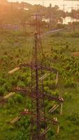 Power line pylons near the river. Electric towers with electric cables with high voltage current. Flight over the transmission lines in the evening. Aerial view. Vertical video