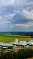 Innovative biogas farm. Biogas power plants on green field under beautiful sky. The agricultural and greenhouse complex is equipped with its own biogas production. Aerial view. Vertical video