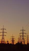 Silhouette of high-voltage towers. Electricity pylons on energy station on the background of beautiful sky at sunset. Electricity station and high-voltage power lines.View from below. Vertical video