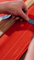 Female's hands are sketching lines with a tape measure and a soap on a table. Sewer works with red fabric and a ruler in atelier. Handicraft concept. Vertical video