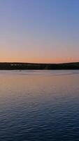 rivière à le coucher du soleil. vol plus de le tranquille l'eau dans le soir. incroyable vue de une calme l'eau en dessous de clair ciel. silhouette de une bateau sur l'eau sur la nature Contexte. verticale video