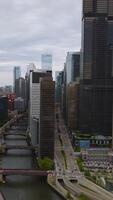Approaching the row of high buildings separating Chicago River from wide busy multi-lane roads. Beautiful architecture of the city on cloudy day. Vertical video