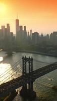 animado tráfico terminado Manhattan puente a dorado hora. maravilloso rascacielos siluetas a fondo de naranja cielo. parte superior vista. vertical video