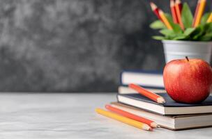 Fresh red apple sits on stacked notebooks in a classroom with colorful pencils in background photo
