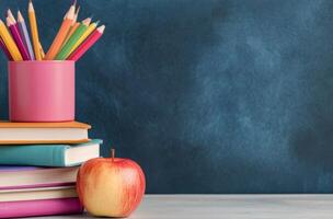 Colorful pencils and an apple on a stack of books against a blue background photo