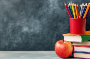 Colorful pencils and an apple on a stack of books against a blue background photo