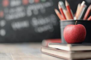 Fresh red apple sits on stacked notebooks in a classroom with colorful pencils in background photo
