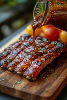 Delicious barbecue ribs being glazed with sauce on a wooden cutting board photo
