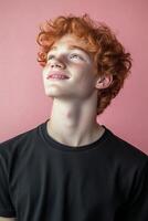 Young man with curly red hair looking up against a pink background photo