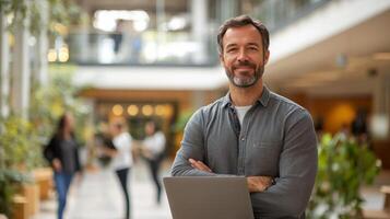 Professional man standing confidently with laptop in a modern office space photo