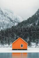 Bright orange cabin surrounded by snowy mountains and trees near frozen lake in winter photo