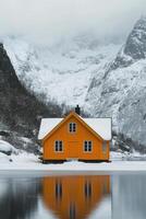 Bright orange cabin surrounded by snowy mountains and trees near frozen lake in winter photo