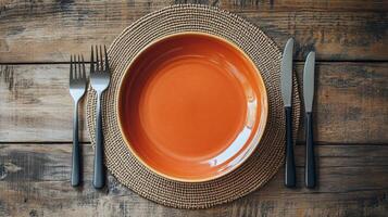 Table setting with orange plate and utensils on a rustic wooden surface photo