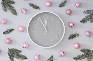 Creative trendy Christmas pattern made with pink Xmas baubles, green snowy Christmas tree branches and gray and white wall clock on gray background. Minimal Christmas eve or New Year idea. Flat lay. photo
