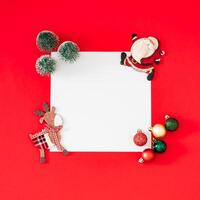 Christmas layout made with green Xmas trees, Christmas baubles, Santa, reindeer decoration and white paper card note copy space on red background. Christmas and New Year concept. Flat lay. photo