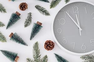Trendy Christmas pattern made with Xmas trees, green snowy Christmas tree branches, pinecones and gray and white wall clock on gray background. Minimal Christmas eve or New Year idea. Flat lay. photo