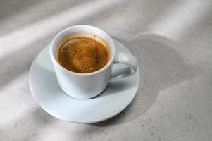 saucer and cup with milk coffee on marble gray table background with natural geometric shadow of sunlight, good morning business branding background photo