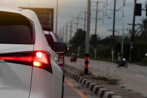 Tail light of white car with wet drop of water. With turn light signal for u-turn on the road. with concrete island on the road and motorcycle reverses in front. photo