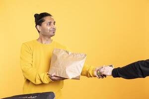 Jolly delivery worker offering groceries order to man paying with debit card. Customer buying meal from upbeat courier, swiping card on POS device, isolated over studio backdrop photo