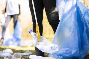 Female environmentalist picking up garbage from the ground to fight pollution within the forest environment, ecological justice. Volunteer doing community service to tidy the woods from rubbish. photo